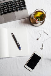 Mobile phone with book and tea by laptop on desk in office - SBDF04282