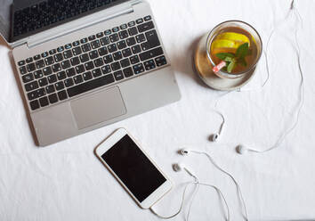 Mobiltelefon mit Kopfhörern und Tee am Laptop auf dem Schreibtisch im Büro - SBDF04283