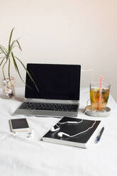 Mobile phone with book and tea by laptop on desk against wall in office - SBDF04284