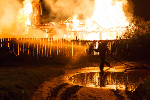 Feuerwehrmann sprüht Wasser aus Schlauch auf brennendes Haus in der Nacht - EYF09405