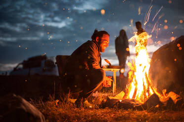 Side View Of Man Crouching By Campfire At Night - EYF09478