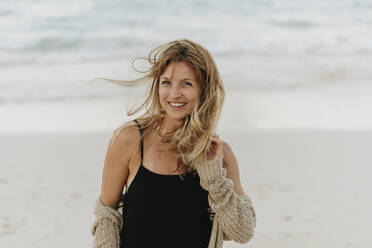 Portrait of smiling mid adult woman with blond hair standing against sea - SMSF00014