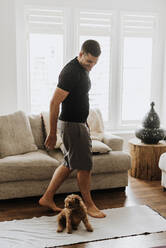 Mid adult man playing with poodle in living room at home - SMSF00022