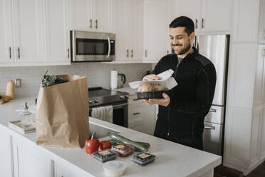 Smiling mid adult man cleaning groceries in kitchen at home - SMSF00029