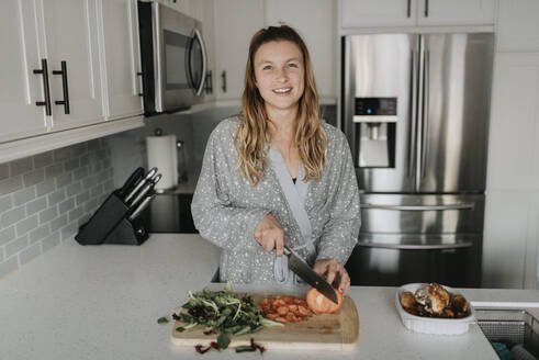 Lächelnde Frau hackt Gemüse auf einem Schneidebrett in der Küche - SMSF00031