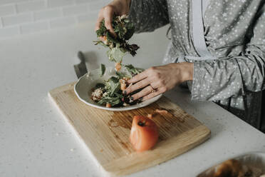 Nahaufnahme einer mittleren erwachsenen Frau, die zu Hause einen Salat auf einem Teller zubereitet - SMSF00032