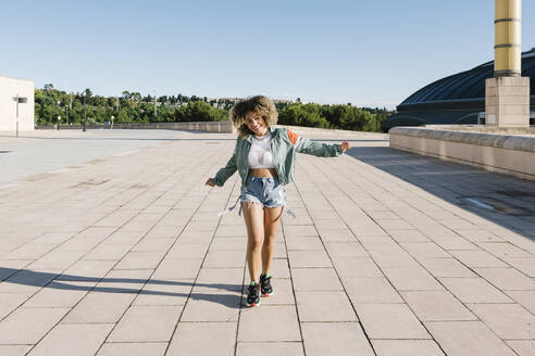 Cheerful fashionable woman walking on city street during sunny day - XLGF00303