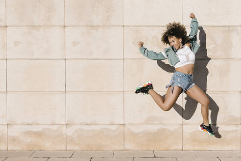 Aufgeregte junge Frau, die an einem sonnigen Tag gegen die Wand springt - XLGF00307
