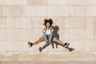 Aufgeregte junge Frau, die schreit, während sie an einem sonnigen Tag gegen die Wand springt - XLGF00308