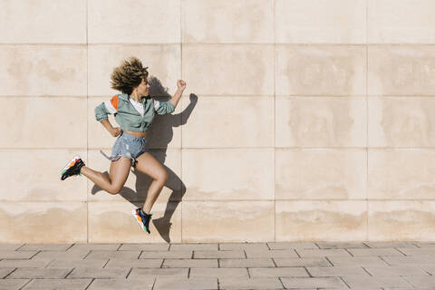 Junge Frau springt an einem sonnigen Tag gegen die Wand, lizenzfreies Stockfoto