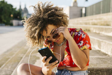 Trendy woman using smart phone while sitting on steps in city - XLGF00317