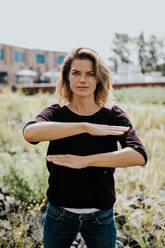 Porträt einer Frau, die auf einem Feld stehend ein Gleichheitszeichen macht - EYF09517