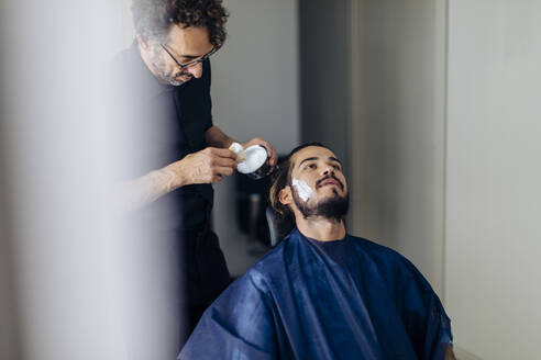 Friseur trägt Rasierschaum auf einen Kunden im Salon auf - SODF00806