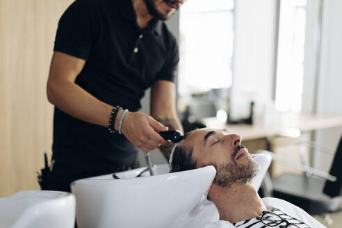 Friseurin wäscht die Haare eines Kunden im Friseursalon - SODF00811