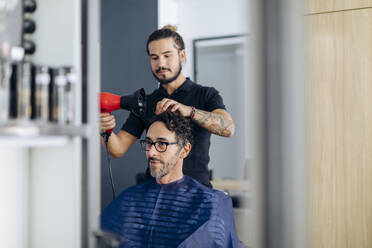 Friseur föhnt die Haare eines Mannes im Salon - SODF00815