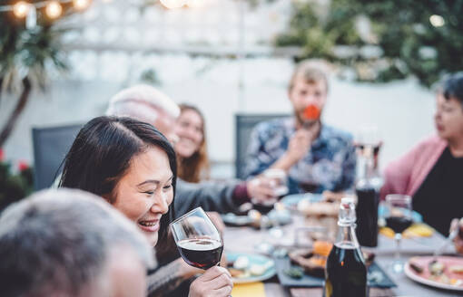 Lächelnde Frau trinkt Rotwein, während sie mit Freunden am Esstisch sitzt - EYF09554