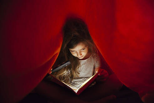 Nahaufnahme von Mädchen mit Handy Licht Lesen Buch unter Decke - EYF09581