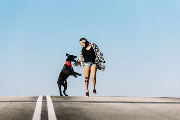 Frau mit Hund und Skateboard gegen klaren blauen Himmel - EYF09583