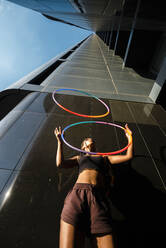 Sportliche junge Frau jongliert mit Plastikreifen vor einem Wolkenkratzer in der Stadt - JMPF00098
