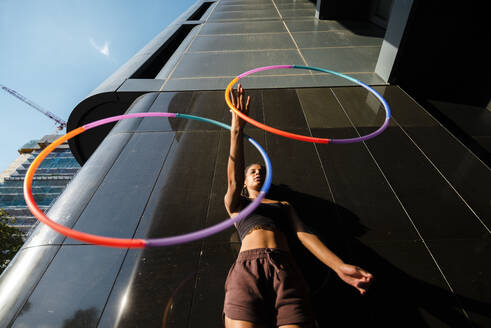 Sporty woman juggling plastic hoops outside modern building in city - JMPF00099