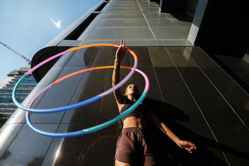 Sporty woman exercising with plastic hoops outside modern building - JMPF00100