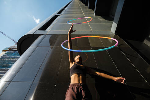 Sporty woman juggling with plastic hoops outside office building - JMPF00101