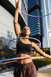 Sportliche Frau, die mit Plastikreifen vor Bürogebäuden trainiert - JMPF00104