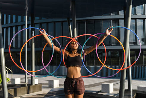 Sportliche Frau, die in der Stadt Plastikreifen auf den Händen balanciert - JMPF00108
