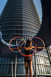 Sportliche Frau balanciert Plastikreifen vor einem modernen Bürogebäude - JMPF00109