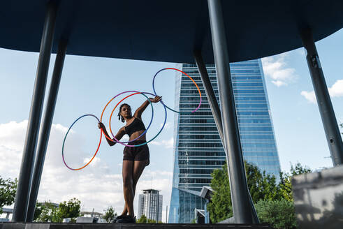 Sporty woman balancing plastic hoops in modern city - JMPF00110