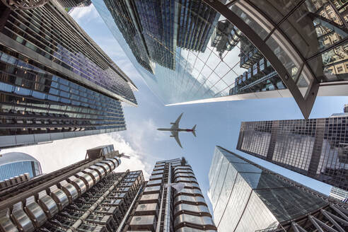 Großbritannien, London, Flugzeug fliegt über moderne Wolkenkratzer an einem sonnigen Tag, Froschperspektive - WPEF03155