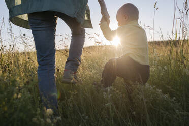 Cute boy holding mother's hand while walking on field during sunny day - EYAF01211