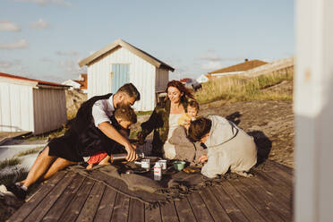 Familie mit Kindern auf einer Decke sitzend vor einer Hütte im Sommer - MASF18418