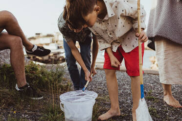 Brother looking at bucket through fishing net while bending by sibling over archipelago - MASF18420