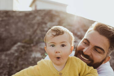 Porträt eines Kleinkindes mit Vater, der lächelnd auf einer Felsformation sitzt - MASF18422