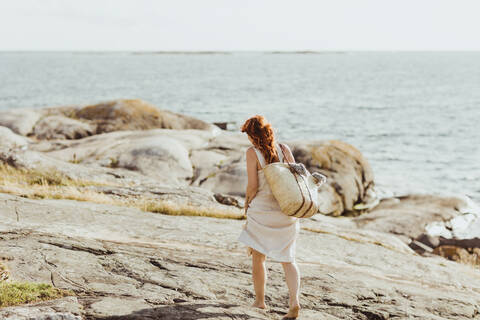 Rückansicht einer Frau mit Tasche, die an einem sonnigen Tag gegen den Himmel läuft, lizenzfreies Stockfoto