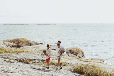 Father with blanket walking by son against sea during summer - MASF18476