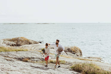 Vater mit Decke, der mit seinem Sohn im Sommer am Meer spazieren geht - MASF18476