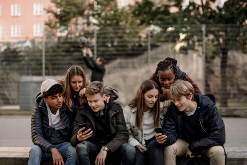 Multiethnische Freunde im Teenageralter benutzen Smartphones, während sie in einem Park in der Stadt sitzen - MASF18501