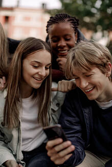 Lächelnder Jugendlicher zeigt Freunden im Park sein Smartphone - MASF18502