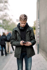 Jugendlicher benutzt Mobiltelefon, während er auf einem Fußweg in der Stadt geht - MASF18510