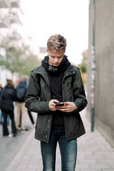 Teenage boy using mobile phone while walking on footpath in city - MASF18510