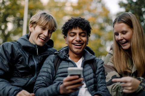 Glücklicher Teenager, der männlichen und weiblichen Freunden in der Stadt sein Smartphone zeigt, lizenzfreies Stockfoto