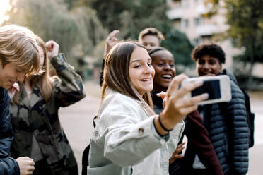 Glückliche multiethnische Freunde machen ein Selfie mit ihrem Handy auf der Straße in der Stadt - MASF18516