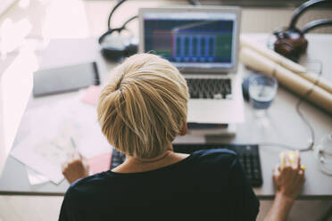 Rückansicht einer Frau bei der Arbeit mit einem Laptop im Büro zu Hause - MASF18631