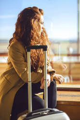 Thoughtful businesswoman sitting on window sill at airport departure area - EHF00381