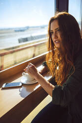 Nachdenkliche Geschäftsfrau rührt Kaffee im Flughafencafé um - EHF00386