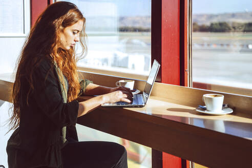 Young businesswoman using laptop while sitting at airport cafe - EHF00394