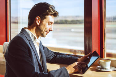 Junger Geschäftsmann benutzt digitales Tablet im Flughafencafé - EHF00396