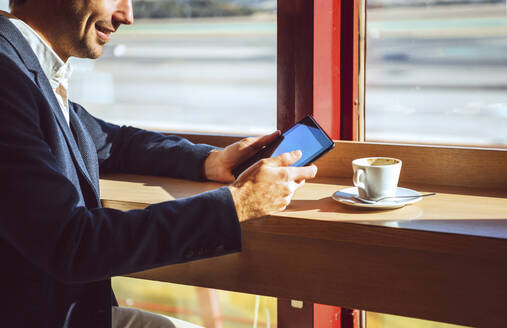 Lächelnder Geschäftsmann mit digitalem Tablet in einem Flughafencafé - EHF00398